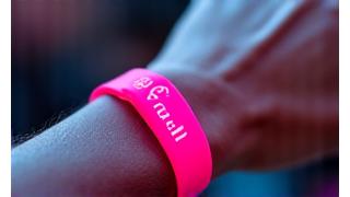 Close-up of a person's wrist wearing an RFID festival wristband, tapping it on a point-of-sale terminal for a cashless payment.